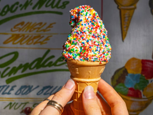 Female hands receiving a soft serve ice cream cone with sugar sprinkles ("100s & 1000s" or sparkles) from ice cream truck: released signage in the background (from Sydney Lypse 2017)