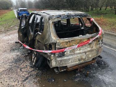 An abandoned burned out car on the road near Crapstone