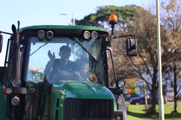 A proud driver and his young passenger wave at the many people lining the country roads last weekend to watch the tractor rally.