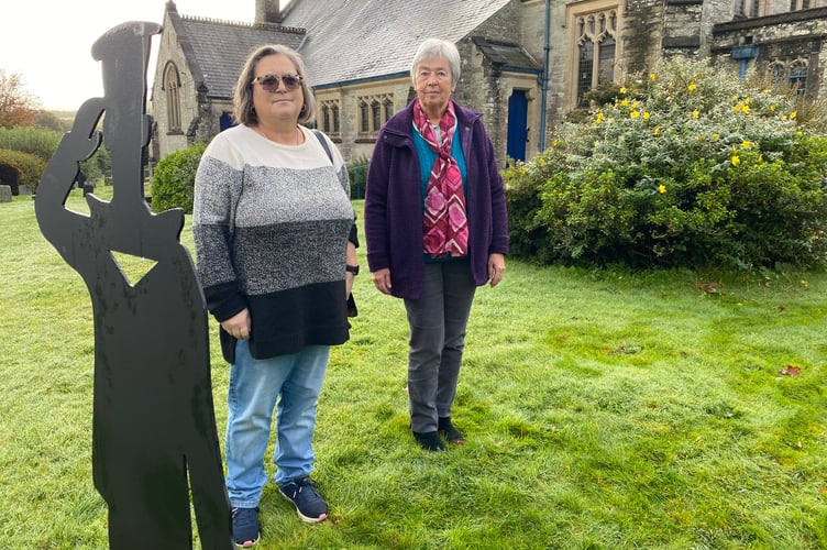 Colette Hutchins and Hilary Prout in Horrabridge Churchyard front of a saluting sailor silhouette in tribute to the fallen.
