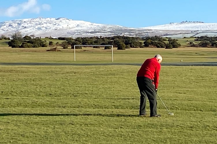 A golfer plays the game on Thursday morning, snow on the hills in the background