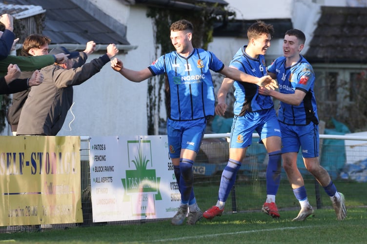 Tom Symons (16) congratulates scorer Harley Sneap (6) whilst Luke Mortimore (11) celebrates with the visiting Tavistock supporters