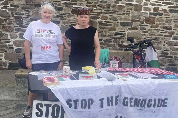 Members of Palestinian Solidarity Okehampton stand behind signs reading 'Stop the genocide, ceasefire now!'.